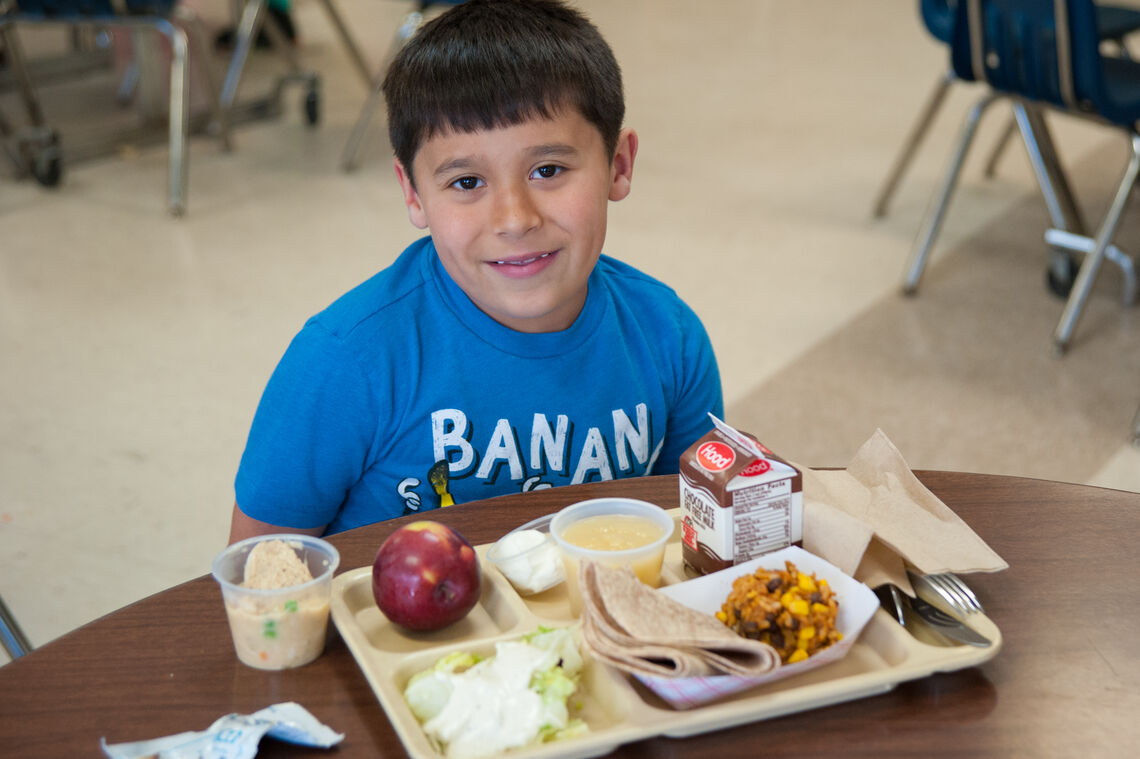 Young Latino boy smiles with mixed rice and bean lunch at school cafeteria table