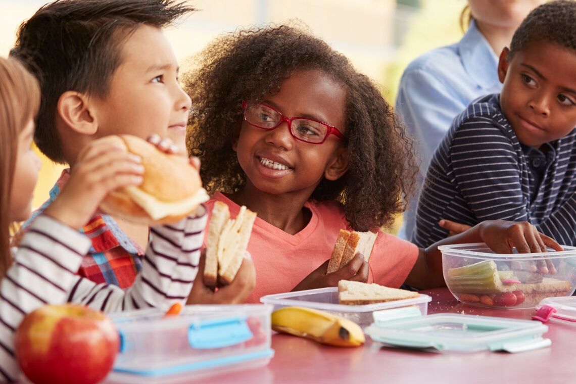Racial and gender diverse group of kids eating school lunch.